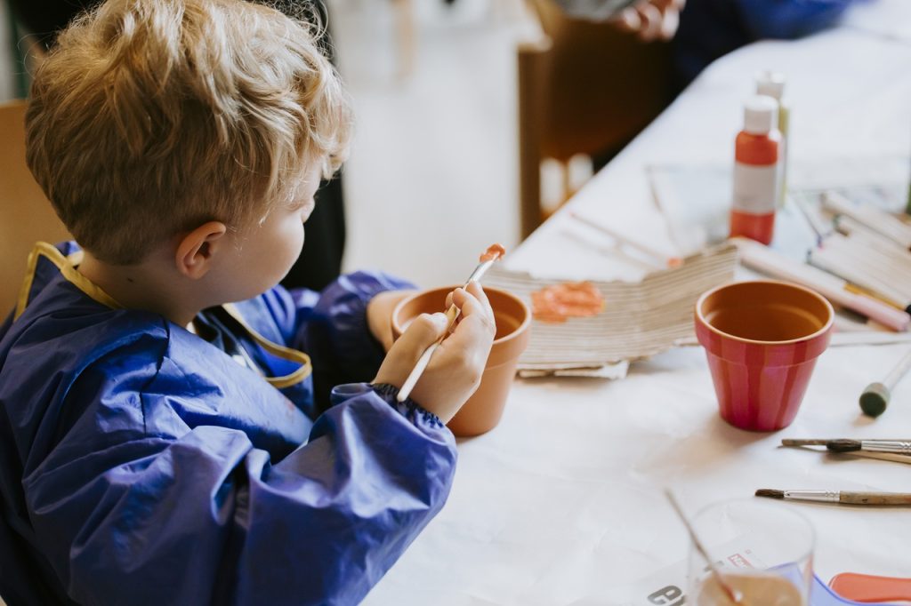 Junger Besucher, der seinen Tontopf kreativ mit Pinsel und Farbe gestaltet